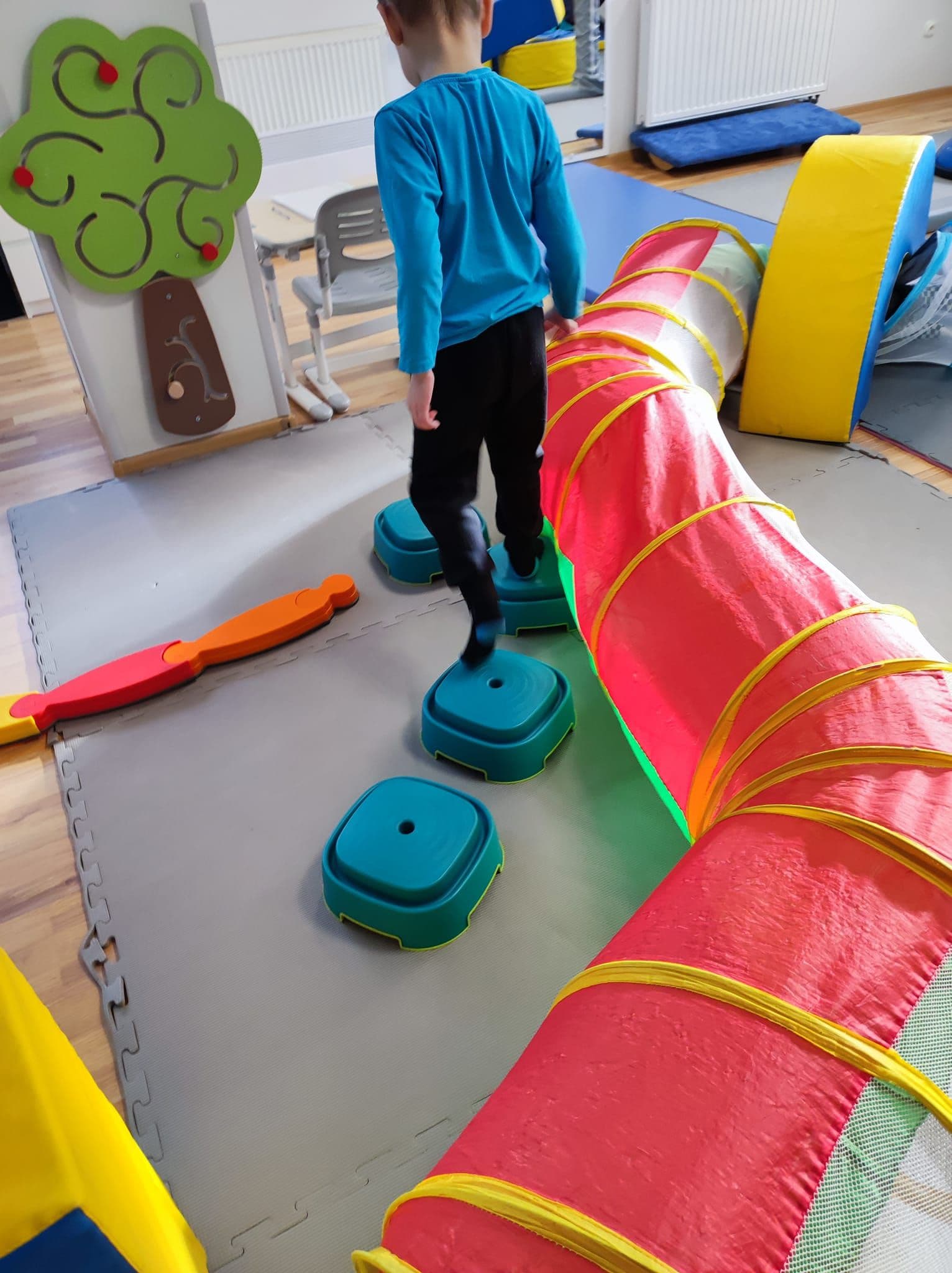 Terapia SI - chłopiec chodzi po klockach równoważnych