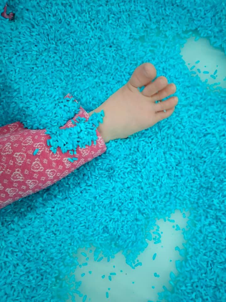 Smyko-multisensoryka - zbliżenie na stopę dziecka umieszczoną w pojemniku z niebieskim pofarbowanym ryżem