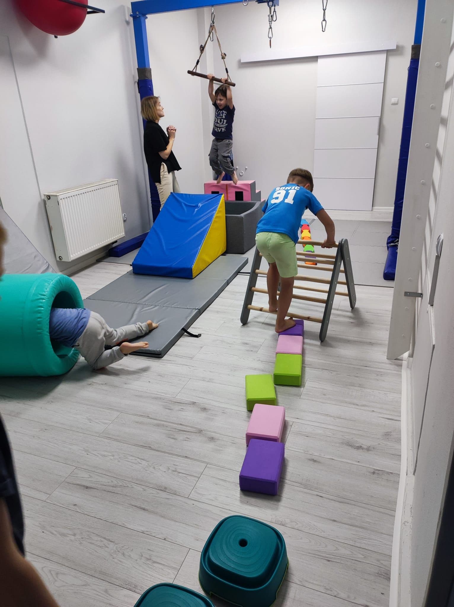 Zdjęcie przedstawia tor przeszkód który pokonuje grupa dzieci podczas zajęć sensoryczno-motorycznych