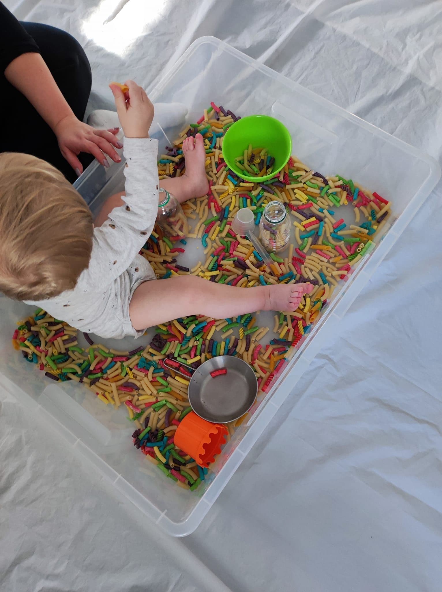 Małe dziecko bawi się kolorowym makaronem podczas zajęć Smyko-multisensoryka